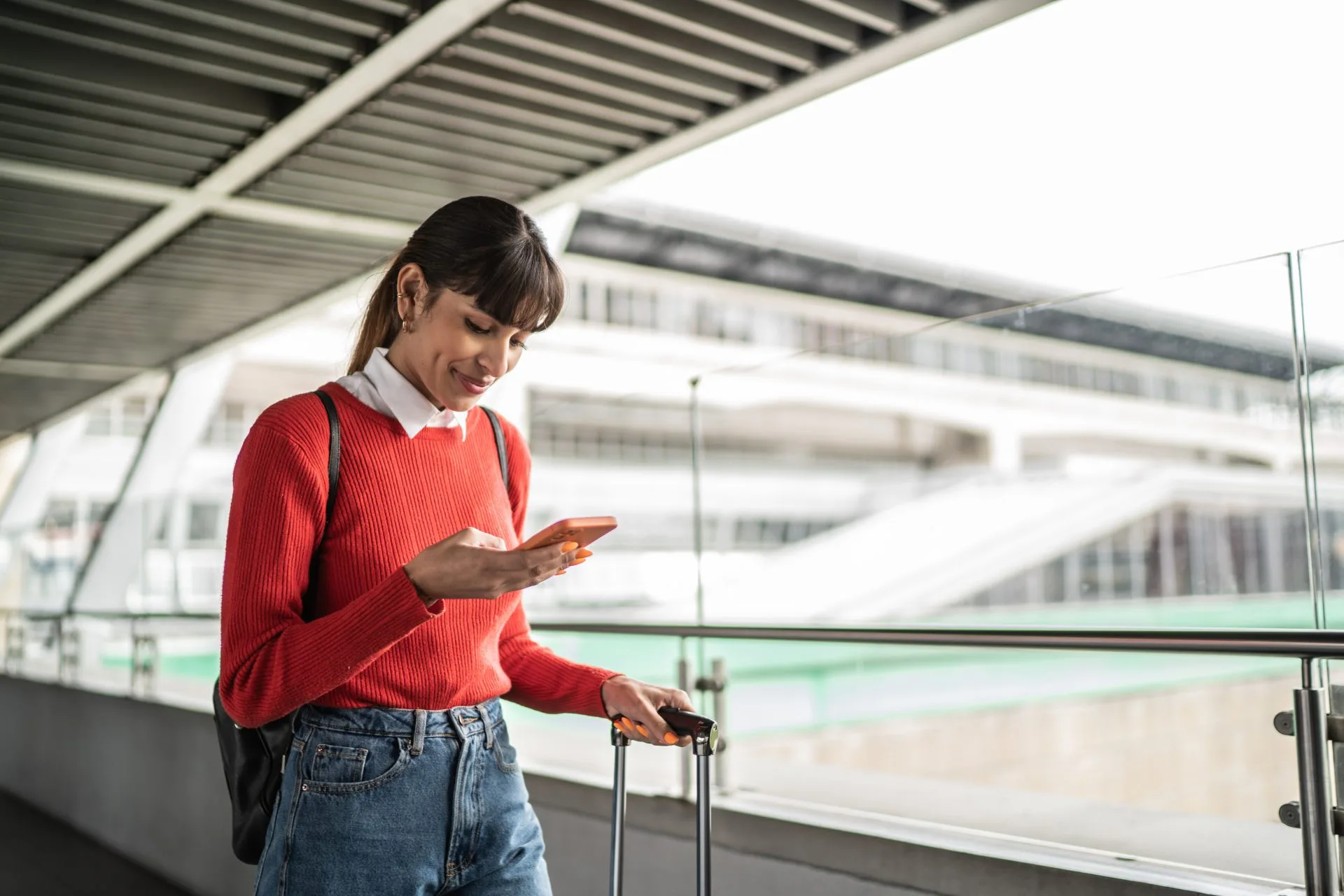 Female traveler pushing a suitcase uses a mobile phone in an airport