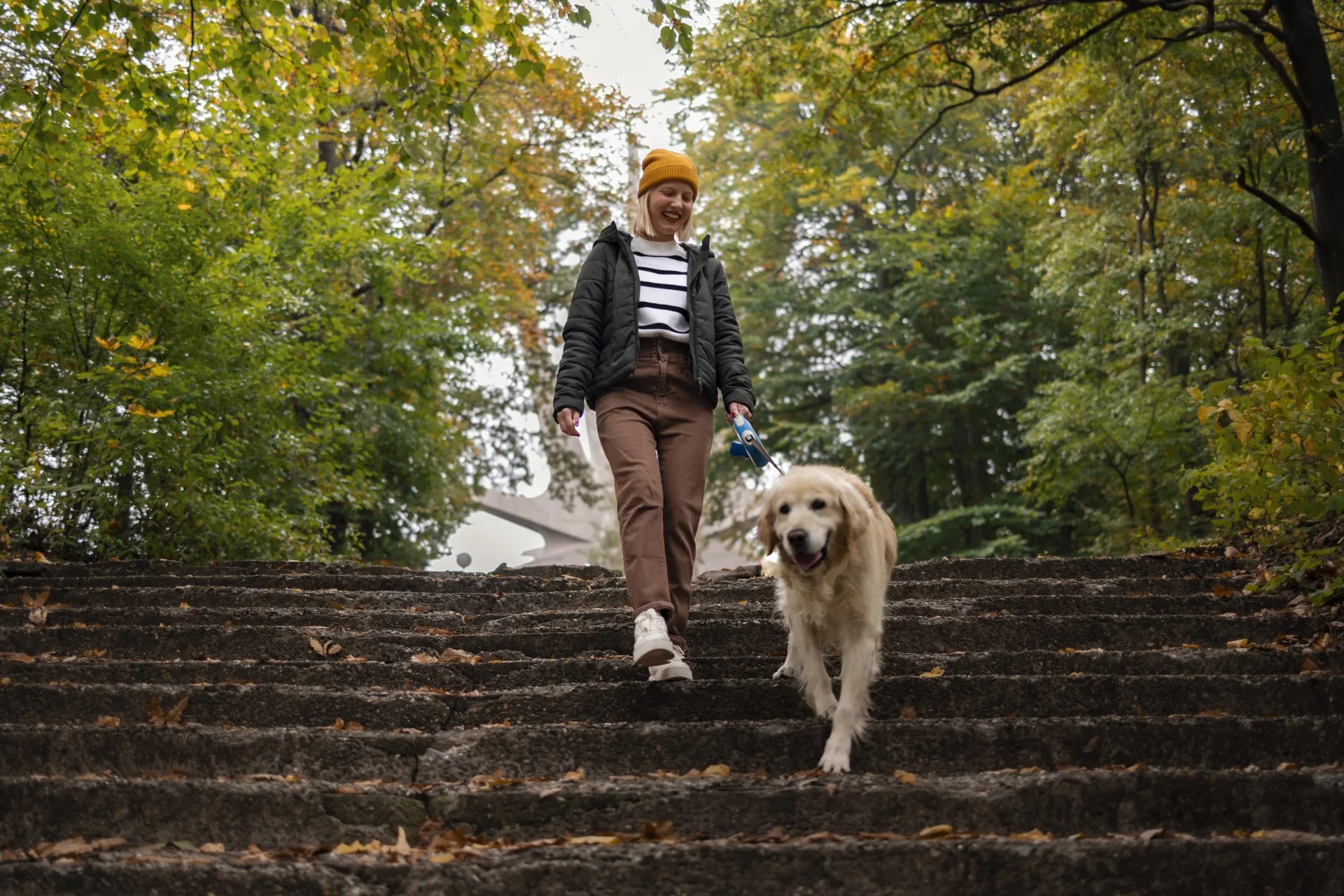 Middle age woman and her dog, a golden retriever, enjoying relaxing walk in nature during autumn.